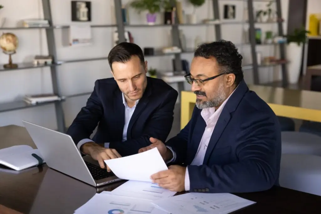 Two financial professionals reviewing printed charts while comparing SatuitCRM vs Monday CRM